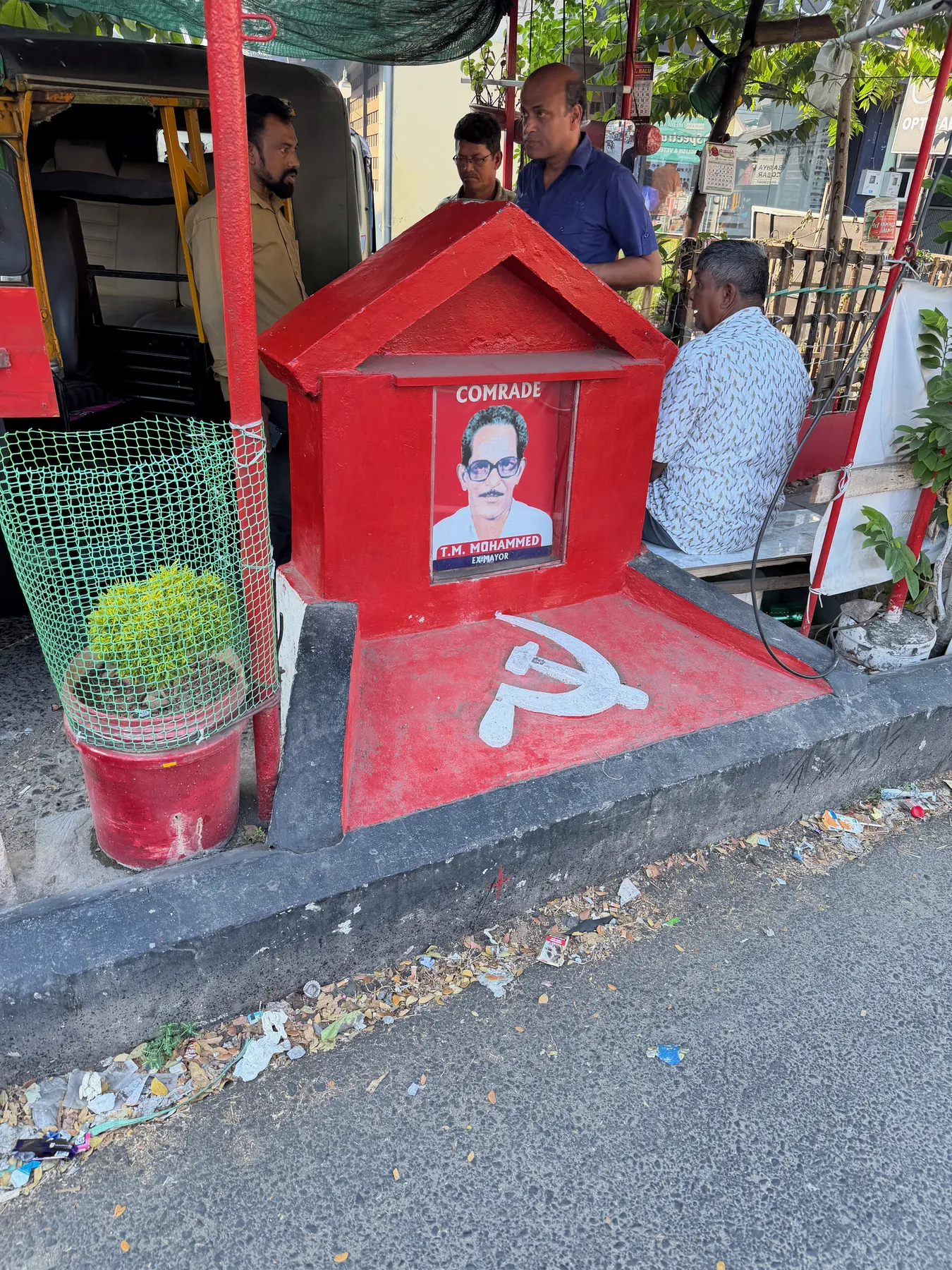 A bright red roadside party booth in Kochi painted with a hammer and sickle and a portrait labeled Comrade