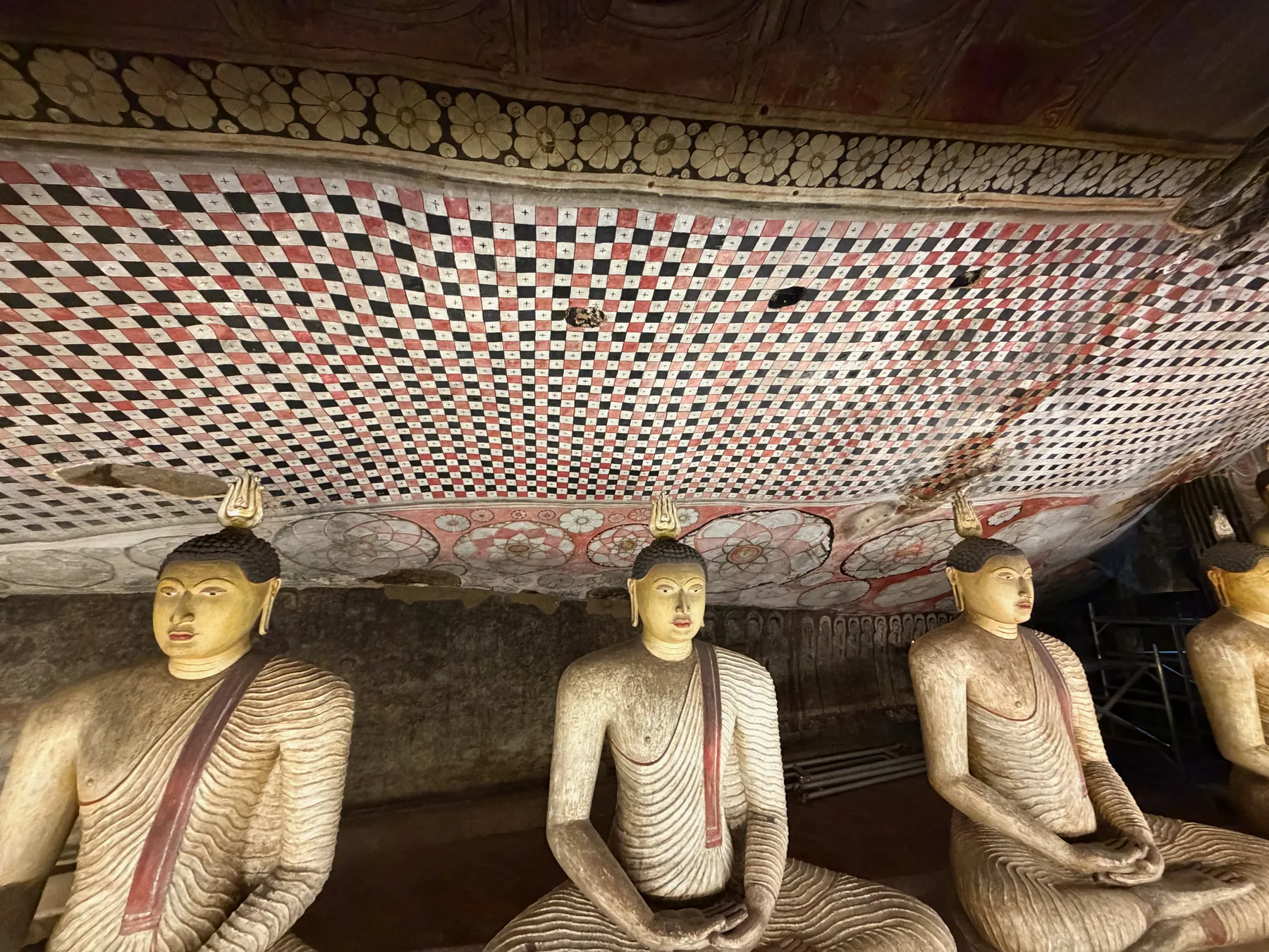 Seated Buddha statues under a painted checkerboard ceiling in the Dambulla cave temples