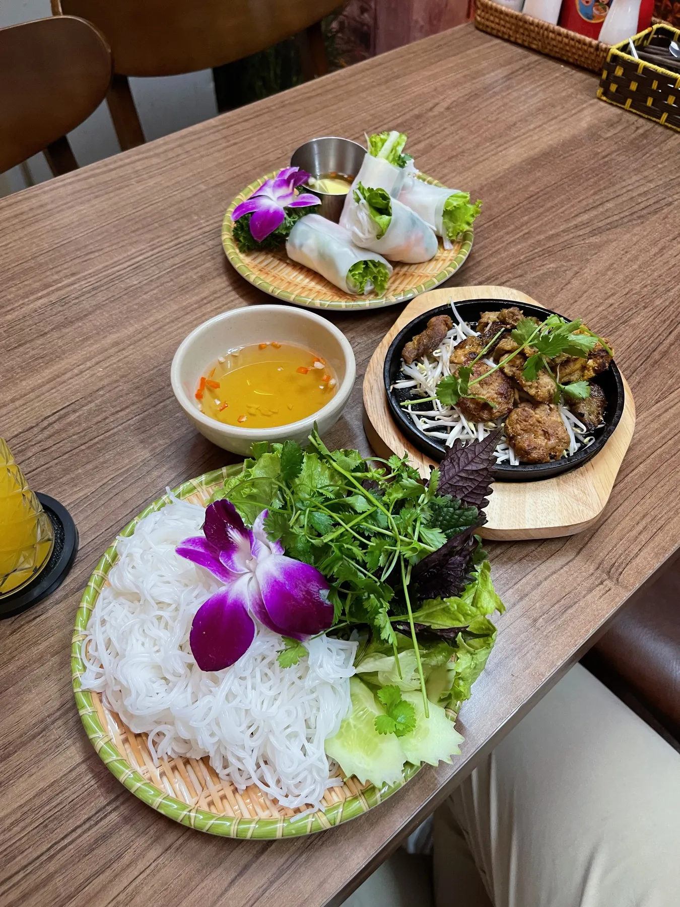 A Hanoi lunch spread of spring rolls, grilled pork, fresh herbs, and vermicelli garnished with orchids