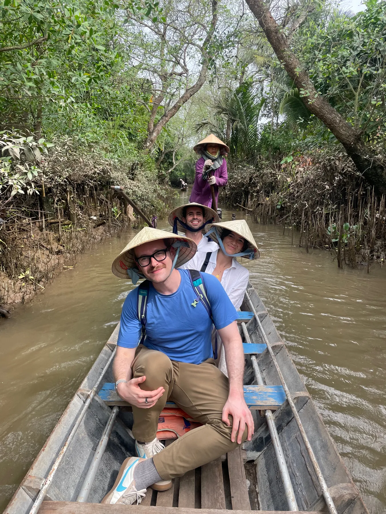 Riding a sampan through a narrow Mekong Delta canal, conical hat and all